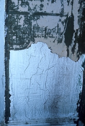 A picture of a wall with peeled paint and a badly cracked wall covering.
