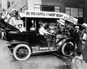 An old, black and white picture from Life Magazine depicting people in an early 20th century car, protesting Prohibition with flags and a banner that reads, "I'm no camel - I want beer."