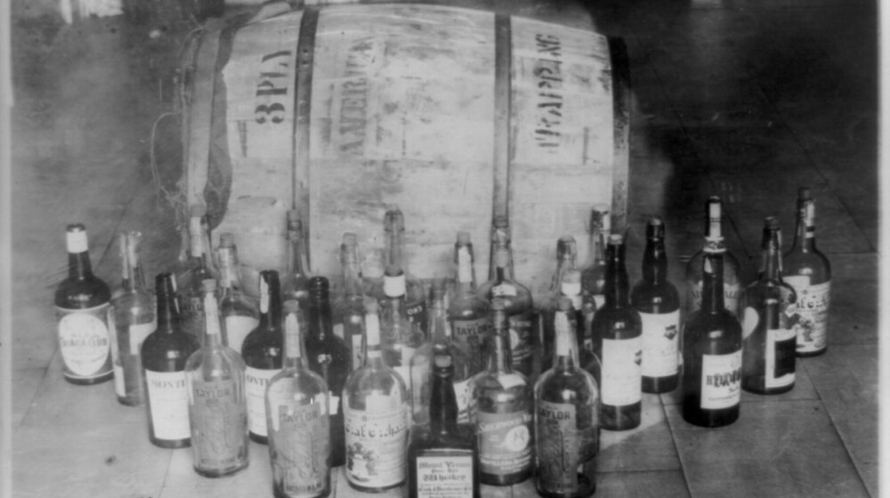 A black and white photo of a wooden barrel and several glass bottles from the Prohibition Era.