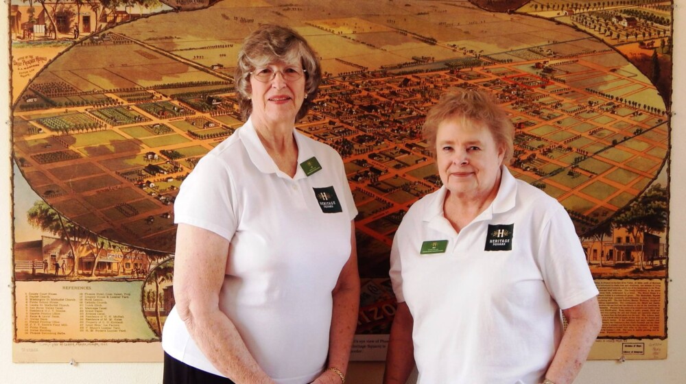 Longtime The Square PHX volunteers Liz and Pat, posing in front of a map of Phoenix from 1895.