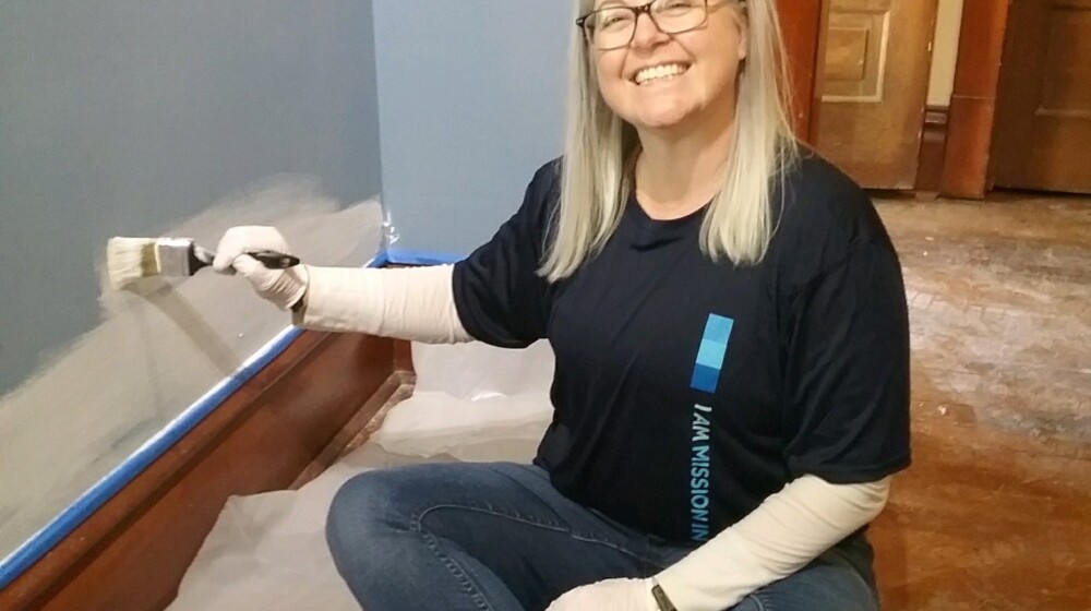 A The Square PHX volunteer smiling as she paints a wall in an exhibit space.