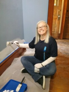 A The Square PHX volunteer smiling as she paints a wall in an exhibit space.