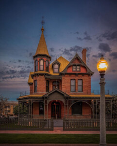 An evening picture of Rosson House, with a fading sunset in a deep blue sky and the lamp in front of the House giving off a golden glow.