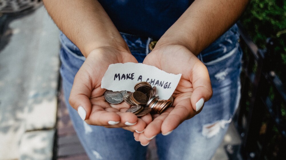 Hands holding coins and a note that says, 