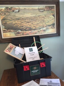 A picture of one of The Square PHX's traveling trunks - the trunk is open and is displaying some of the educational activities, with a wash board, an 19th century game, pictures from the turn of the century, a teachers' binder, and a map of Phoenix in the background circa 1885.