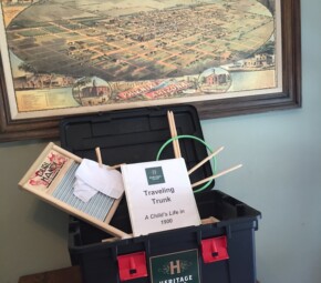 A picture of one of The Square PHX's traveling trunks - the trunk is open and is displaying some of the educational activities, with a wash board, an 19th century game, pictures from the turn of the century, a teachers' binder, and a map of Phoenix in the background circa 1885.