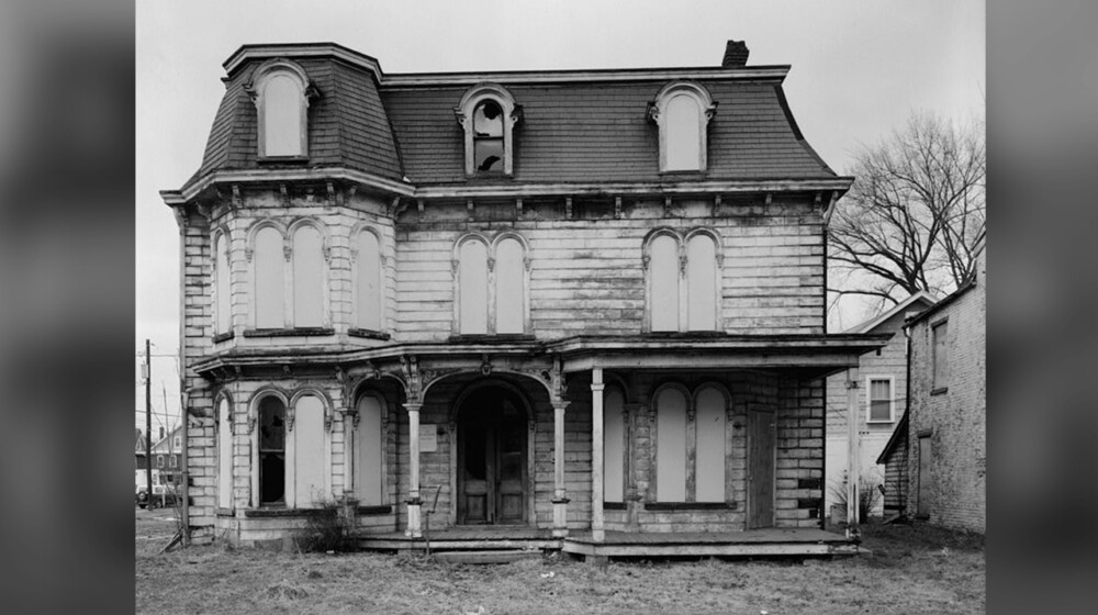 A black and white photo of an old, rundown Victorian era home.