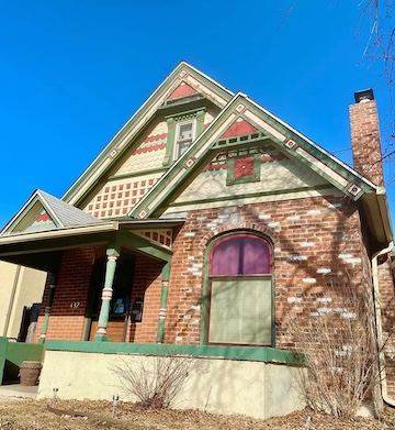 A picture of an older brick home with vibrant green trim and a bright blue sky.