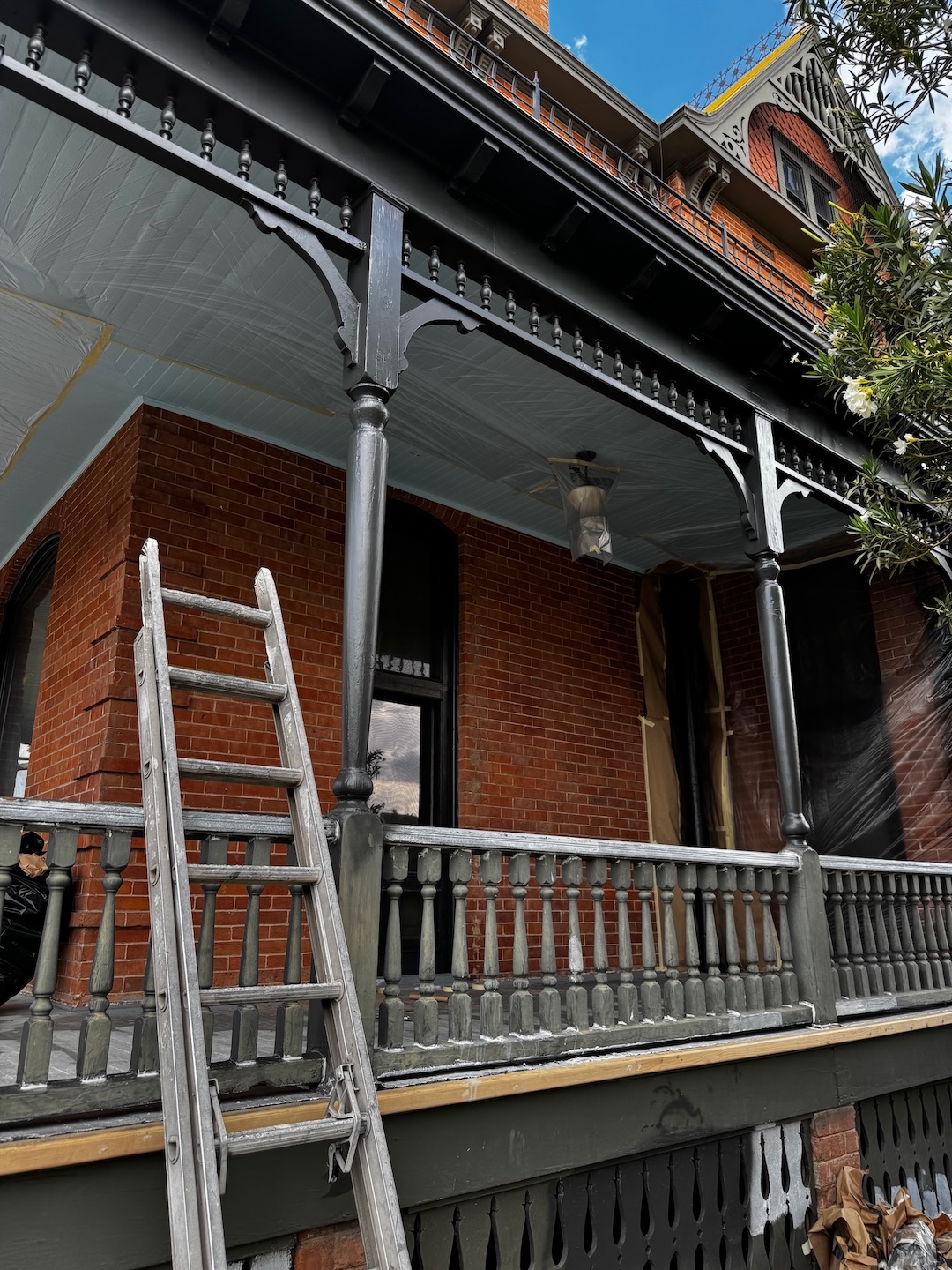 A brick Victorian Era house with construction work being done on the wide front porch.