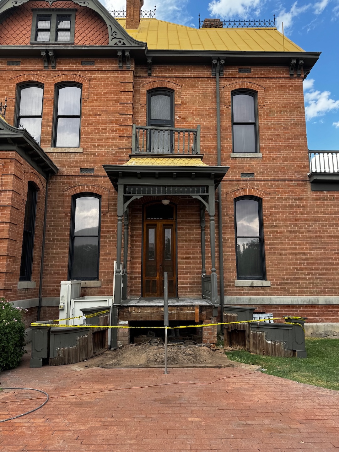 A brick Victorian Era house with construction work being done on a smaller side porch.