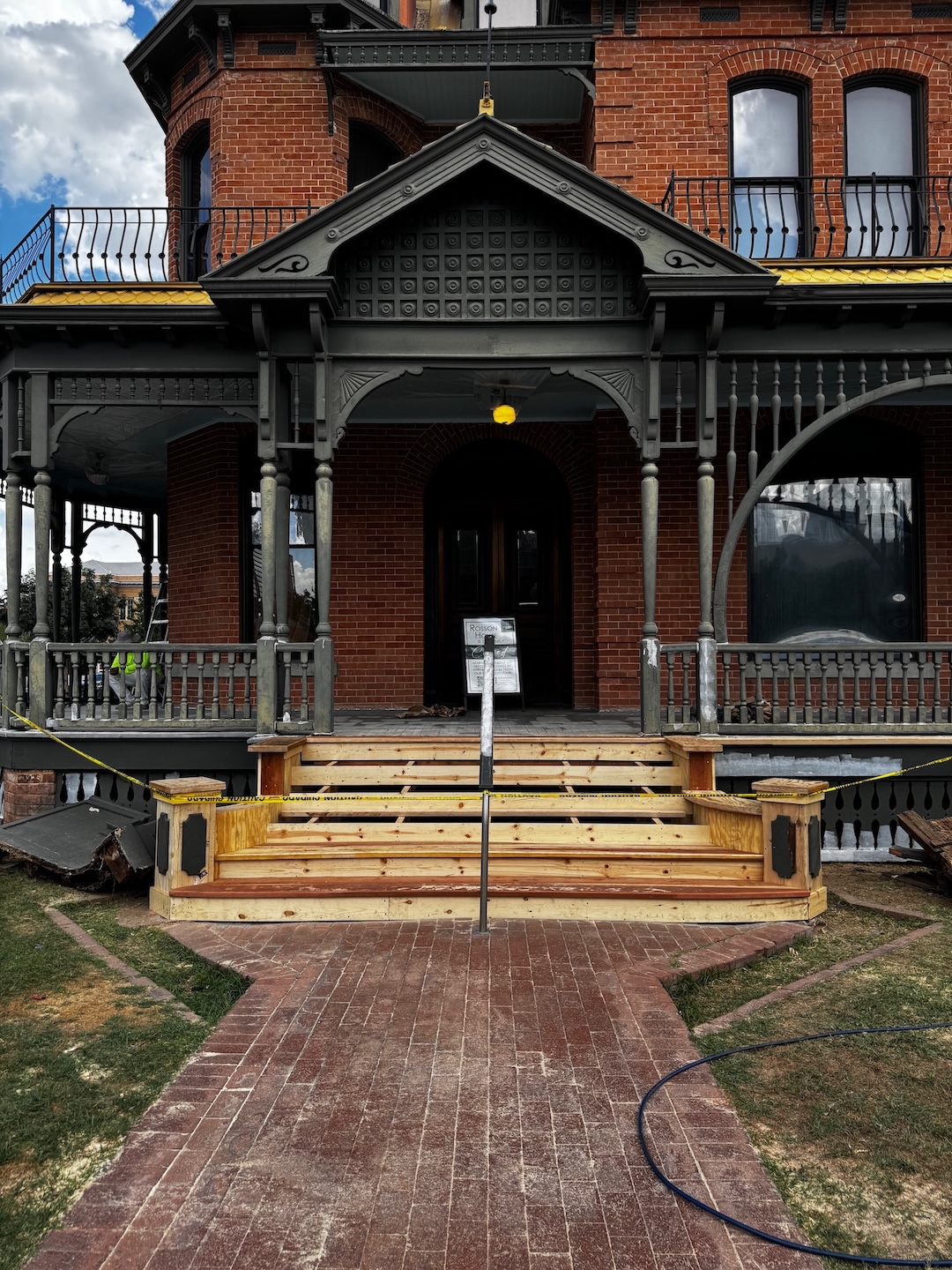 A brick Victorian Era house with construction work being done on the wide front porch.