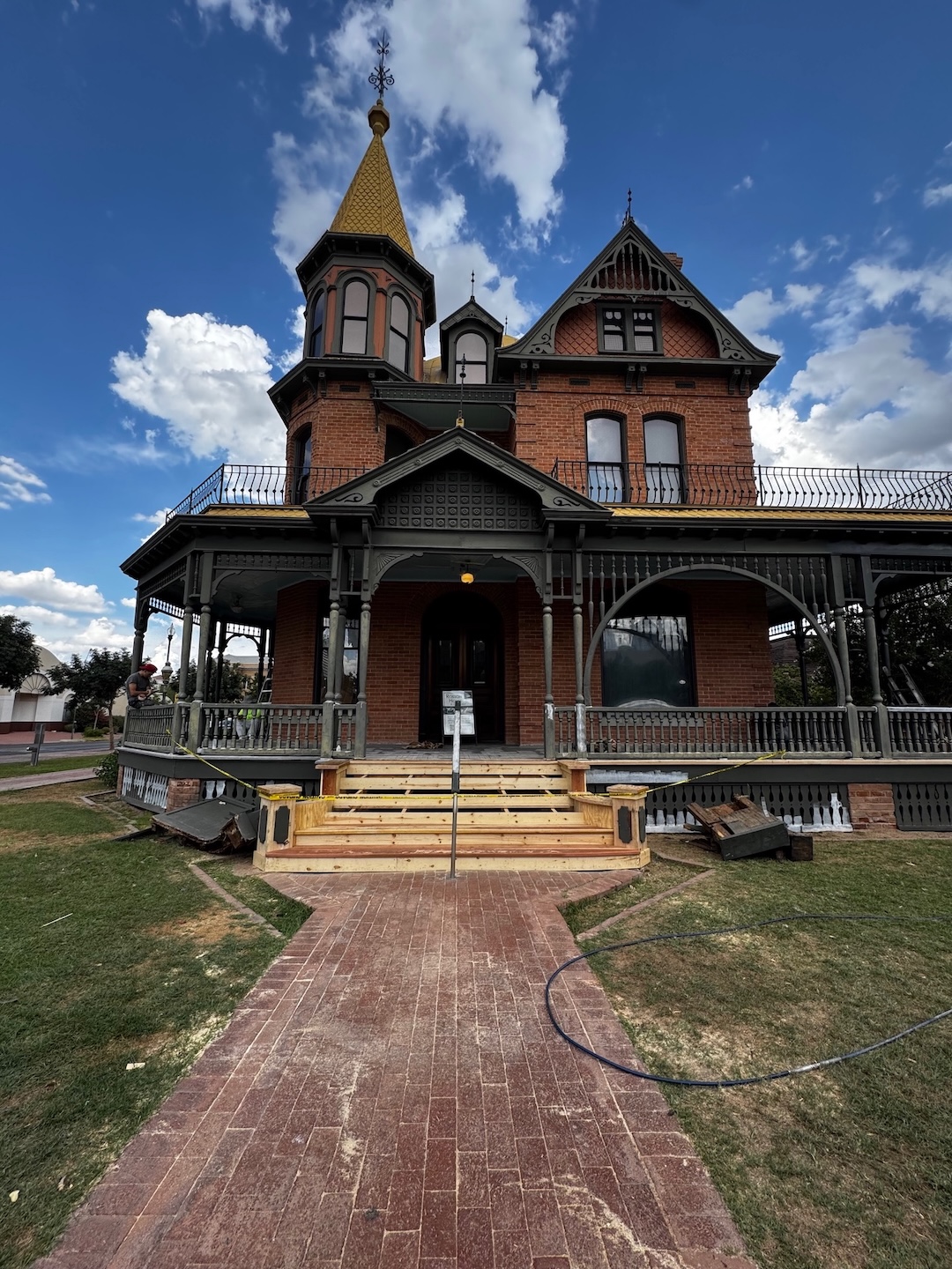 A brick Victorian Era house with construction work being done on the wide front porch.