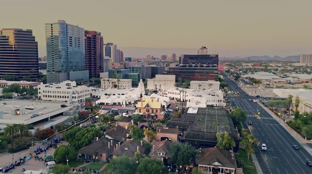 A birds-eye photograph of Heritage and Science Park in downtown Phoenix, showing a combination of modern and historic buildings, green grass and trees, and people attending a festival.